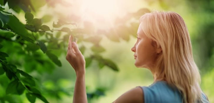 young woman looking at leaves in the forest on sunny summer day