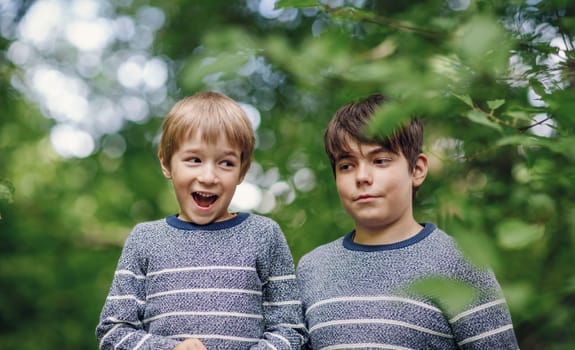 Two lovely happy brothers sitting in park. Boys outdoors in nature