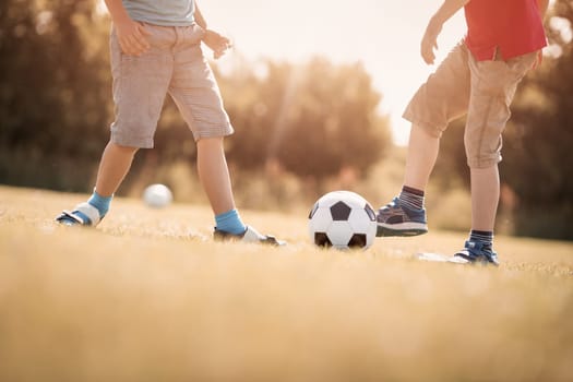 Boys playing football on the field with gates. Active children in summer with ball