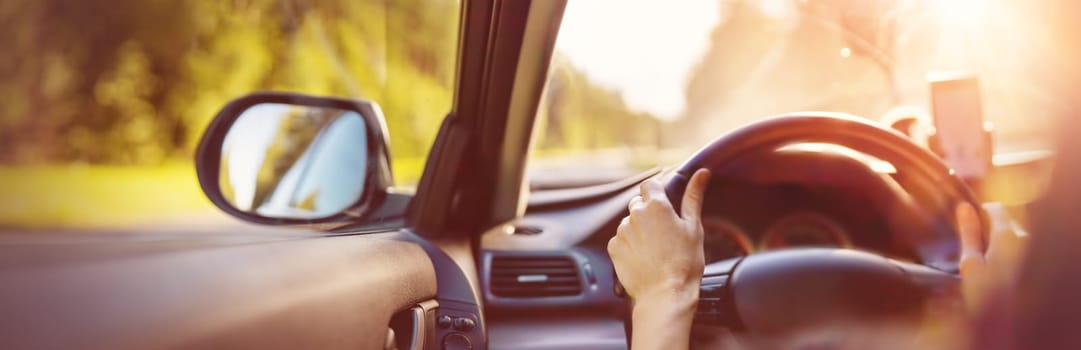 Driver driving a car on asphalt road in summer day at park. Woman at steering wheel