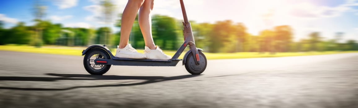 Woman riding on scooter in park in summer. Urban eco transportation