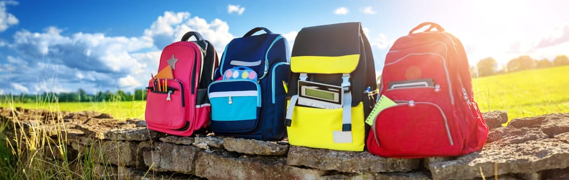 Colourful children schoolbags outdoors on the field. Backpacks with school accessories