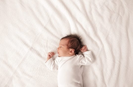 Cute newborn baby girl lying in the bed. Two weeks old infant child on white soft blanket