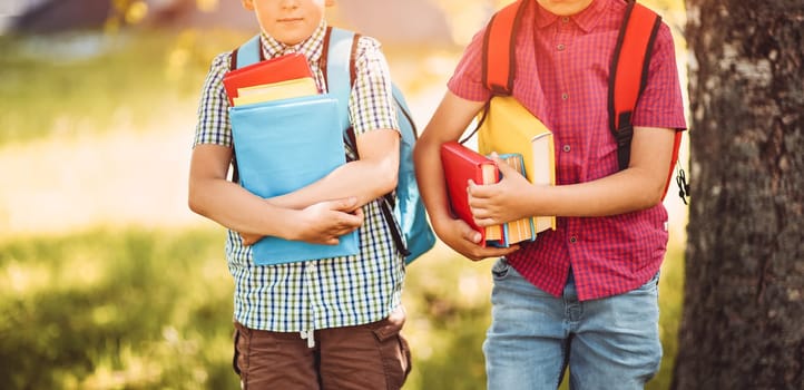 Children with rucksacks standing in the park near school. Pupils with books and backpacks outdoors