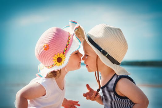 Babygirl and babyboy kissing on the beach in straw hats