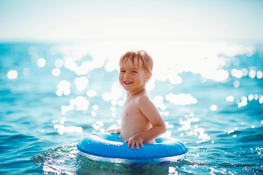 three years old boy playing at the beach with swimming ring. Child on family vacations at sea