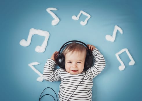 happy little boy on blue blanket background with headphones and musical notes on blue background