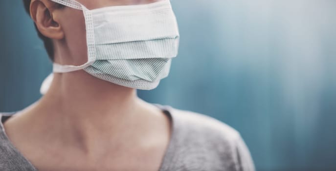 young woman in medical face protection mask indoors on blue background. Sick person