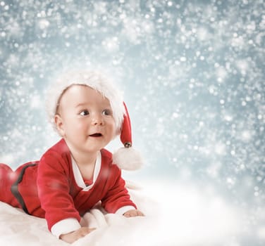 Eight month old baby in knitted winter hat lying on soft blanket with blue background and falling snow