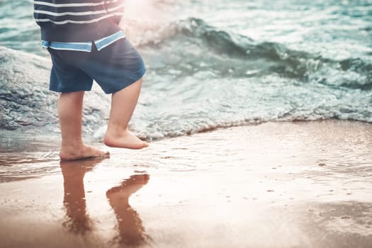 Baby boy barefoot are walking on the beach in water. Child on vacation in summer at the sea on bad weather
