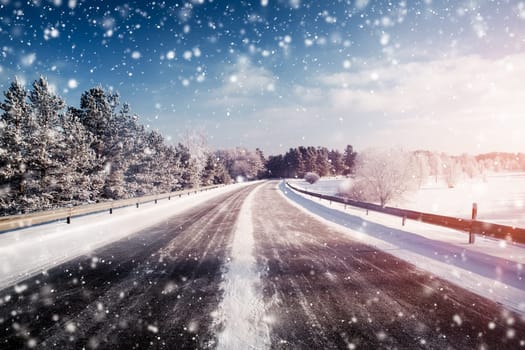 winter road, covered with snow on sunny day. Black icy asphalt