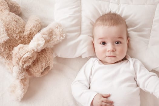 seven month old boy lying in the bed with a plush dog toy