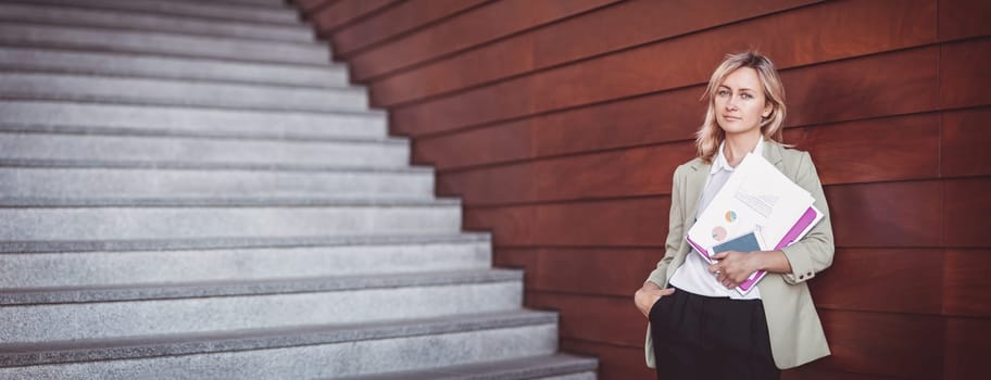 young woman with laptop standing on the stairs. Person with personal computer and documents outdoors