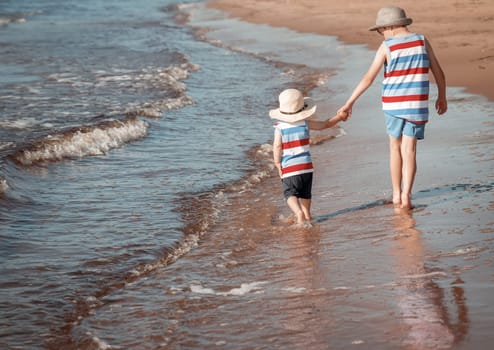 Two brothers barefoot are walking on the beach in water. Boys are on vacation in summer at the sea