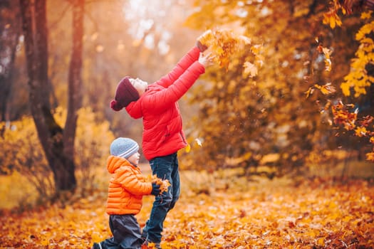 children throwing leaves in beautiful autumnal day. Boys playing outdoors in the park