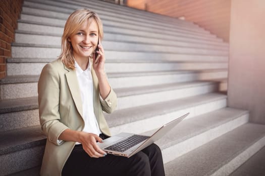 happy young woman with laptop and smartphone sitting on the stairs. Person using personal computer outdoors