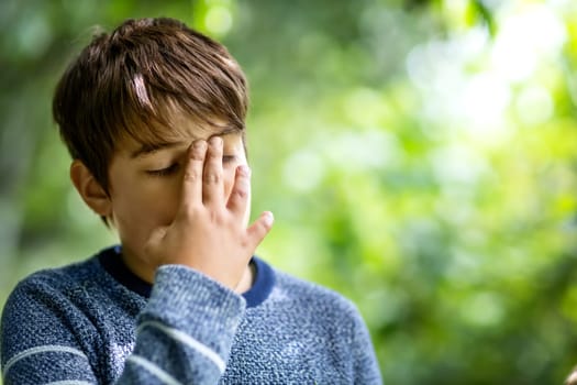 child with headache. Upset young boy outdoors in nature