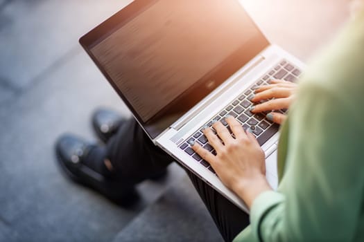 young woman with laptop sitting on the stairs. Person using personal computer outdoors