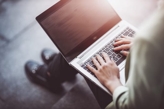 young woman typing on laptop and sitting on the stairs. Person using personal computer outdoors