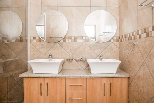 The interior of the bathroom of a brand new house, showing the double basins, mirrors and shower screen.
