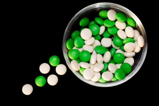 Green and white mints on a glass bowl, and some outside on the black background