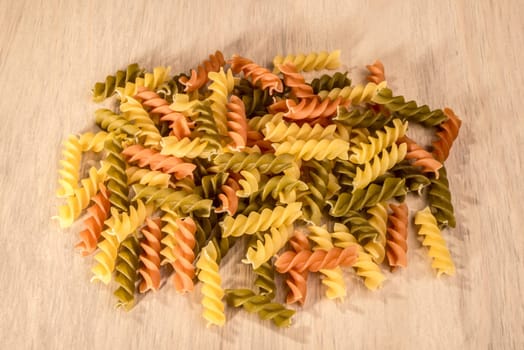 A small heap of three different colours of fussili ly on a wooden table.