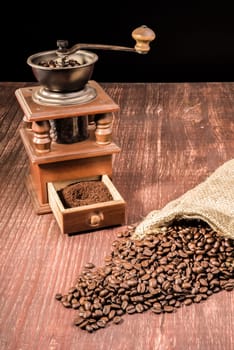 Coffee beans ly spilled from a hessian bag on a wooden table with an old grinder in the back.