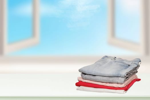 Stack of jeans. Closeup of a pile of colorful female denim pants on a bright table against abstract blurred cloudy sky. Space for your product display montage.