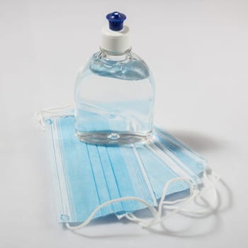 Alcohol gel hand sanitizer and disposable hygienic mask on gray background