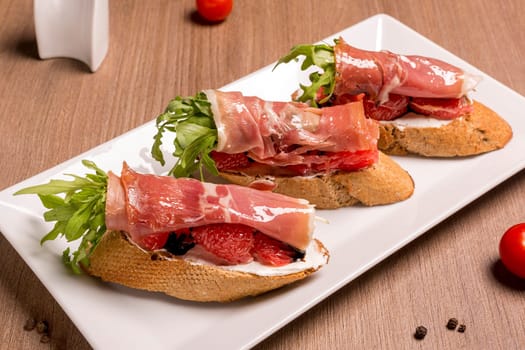 Bruschettes with jamon and grapefruit dried rye baguette, cream cheese, dor-blue, jamon, grapefruit, arugula, balsamic cream. Close-up.