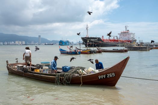 George Town, Penang/Malaysia - Jun 27 2017: Crows fly nearby the fisherman boat. Background is KOMTAR building, ferry, and vessel ship.