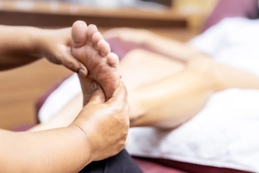 Close up asian woman do foot massage at home with face mask while city lockdown for social distance due to coronavirus pandemic. Massage is one of service business that shutdown while city lockdown.