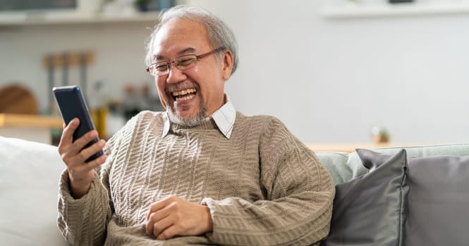 Panoramic Happy retirement elderly man sitting on sofa at living room use cellphone to make video call to his family with laugh and smile. Communication Technology with senior people at home.