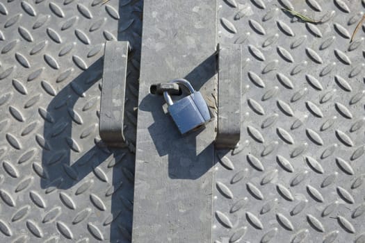 Checkered diamond patterned galvanized steel plates, lit by natural sunlight in an outdoor setting. Shiny metal padlock sits between the two handles
