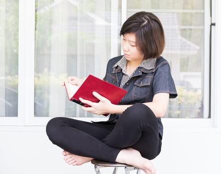 Asian girl with short hair reading a book sitting on a chair