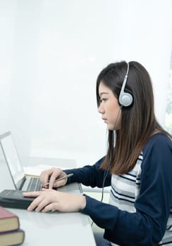 Young female long hair sitting in living room and wearing headphones learning online using laptop at desk .E-learning concept