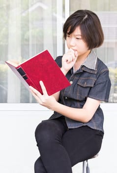 Asian girl with short hair reading a book sitting on a chair