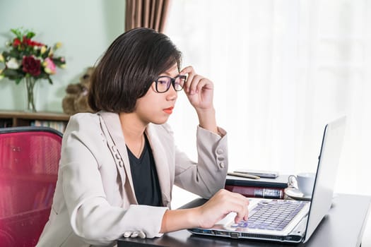 Young asian woman short hair in smart casual wear working on laptop while sitting near window in home office