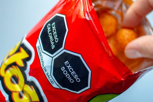 Calgary, Alberta. Canada. Nov 11 2020. Close up to a high sodium and calories warning signs on a bag of cheetos and a person eating.