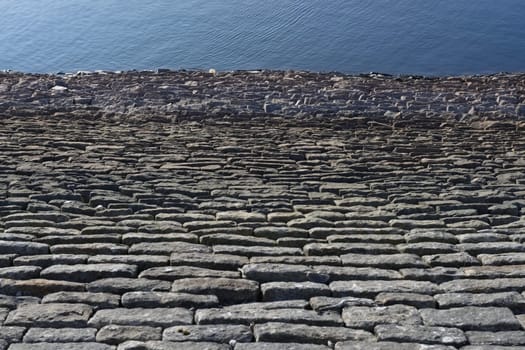 Looking down a sloping reservoir stone wall, a full frame abstract texture image is formed. Deep blue water ripples form good copy space.