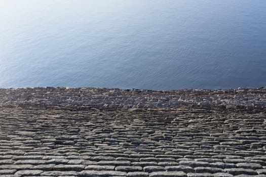 Half and half full frame background texture. Bright blue sunny reservoir water against warm grey linear rock wall. Plain with loads of copy space