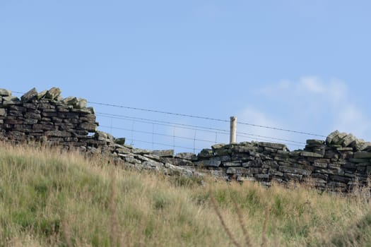 Profile of drystone wall and barbed wire fence against pastel blue sky background. Autumn rural season in the peak district, selective focus texture.