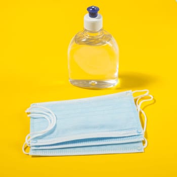 Alcohol gel hand sanitizer and disposable hygienic mask on yellow background