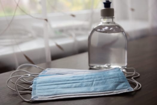 Alcohol gel hand sanitizer and disposable hygienic mask on table