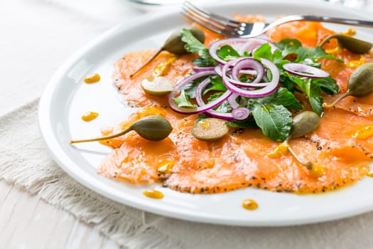 Salmon carpaccio and arugula salad with onions and capers on white plate