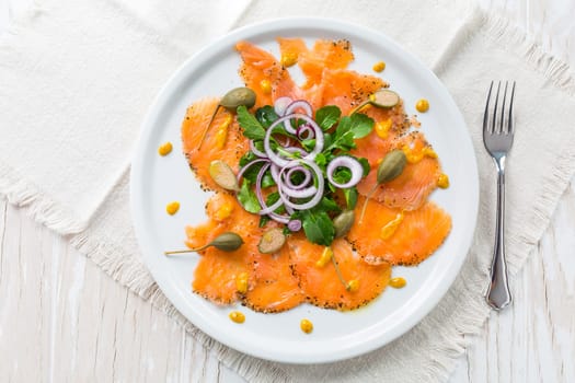 Salmon carpaccio and arugula salad with onions and capers on white plate