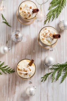 Traditional eggnog with cinnamon and nutmeg for Christmas and winter holidays. With Xmas decorations on wooden background.