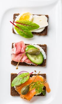 Variation of healthy open sandwiches on Pumpernickel bread with vegetables, salmon, ham, herbs and soft cheese