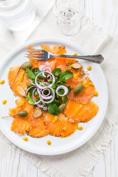 Salmon carpaccio and arugula salad with onions and capers on white plate