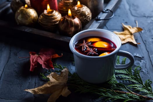 Mulled wine with orange, cinnamon and anise in mug with Christmas ornaments and candles